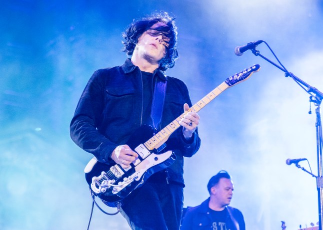 Jack White playing guitar and singing into a microphone stand onstage